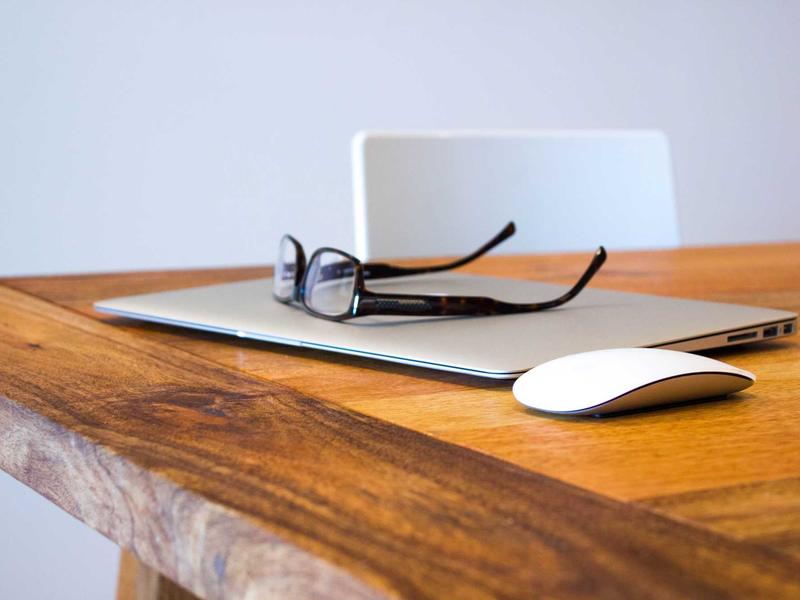 Notebook, Brille und Maus auf hellem Holztisch